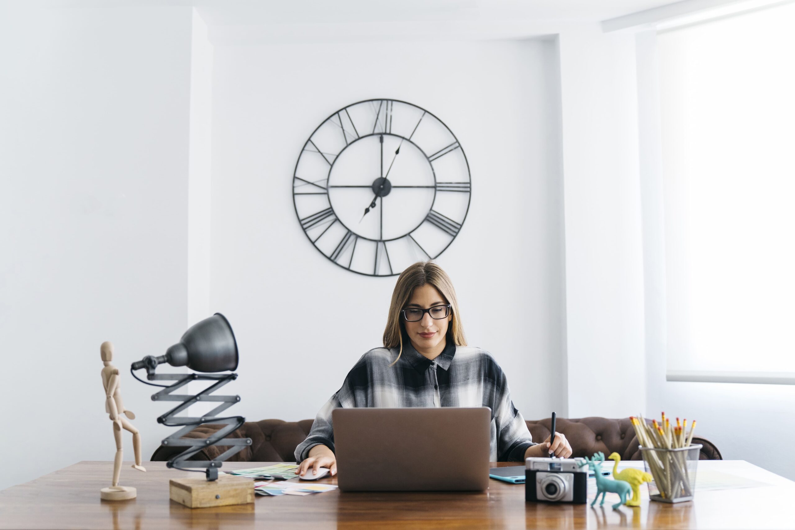 How to Manage Time Zone Difference in Outsourcing - woman working on her laptop in a different time zone with a giant clock behind her